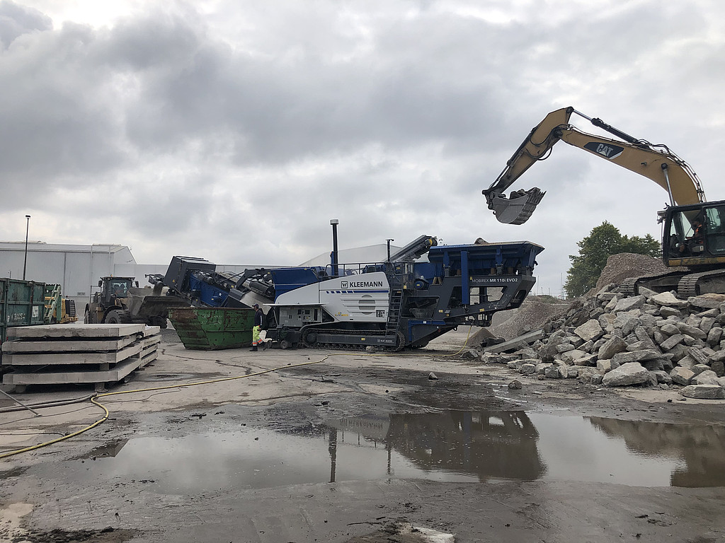 Ein Kran füllt Bauschutt in eine große Maschine